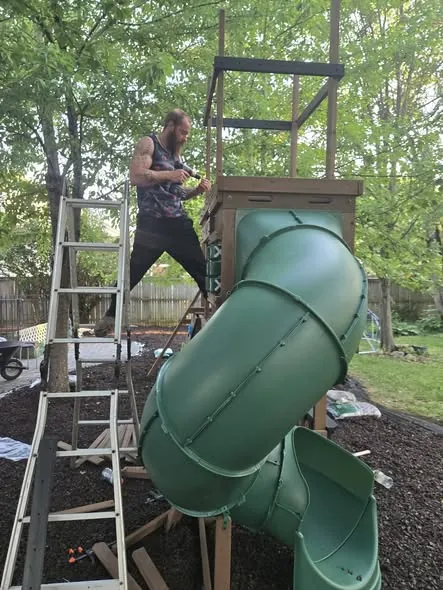 Noah Dean on a ladder assembling a playset tower